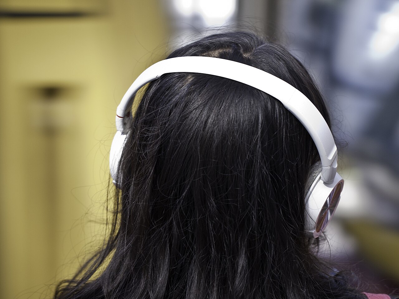 Personne vue de dos portant un casque audio blanc, photographie d’illustration de l’écoute sonore.